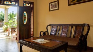 A room with a wooden table, a cushioned bench, a door with a decorative glass panel, and a framed picture on the wall. - OYO 92430 Anora Homestay (Medan)
