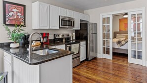A modern kitchen with white cabinets, stainless steel appliances, a granite countertop, and a potted plant. - Cozy Convenient downtown Condo (Wilmington)
