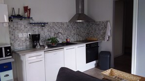 A compact kitchen with white cabinets, a black dishwasher, a stainless steel range hood, and a patterned backsplash. - Pretty little house, in a quiet private courtyard 5 minutes from the sea (Luc-sur-Mer)