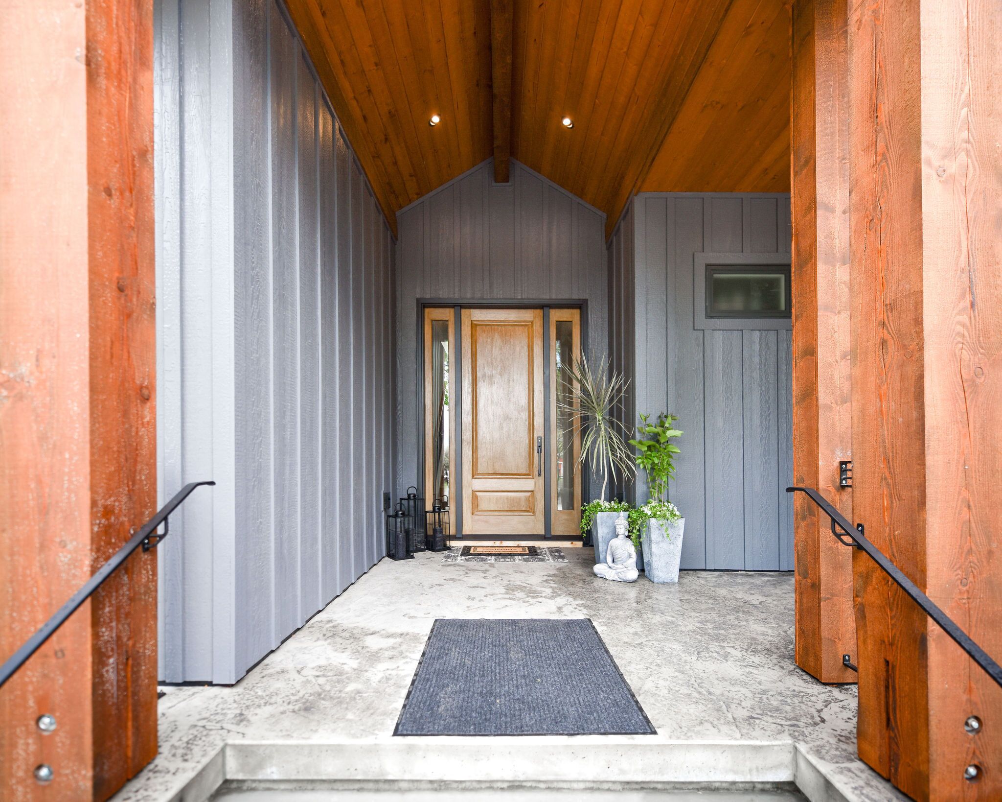 Un intérieur en bois avec une porte, des plantes en pot et un paillasson à l’entrée.