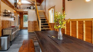 A wooden interior with a dining table, a vase with flowers, a staircase, and a bear head mounted on the wall. - Red Cariboo Resort (Anahim Lake)