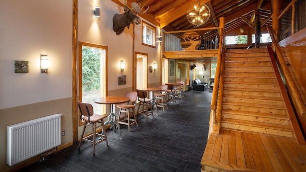 A wooden interior with a staircase, tables, chairs, and a mounted moose head. - Red Cariboo Resort (Anahim Lake)