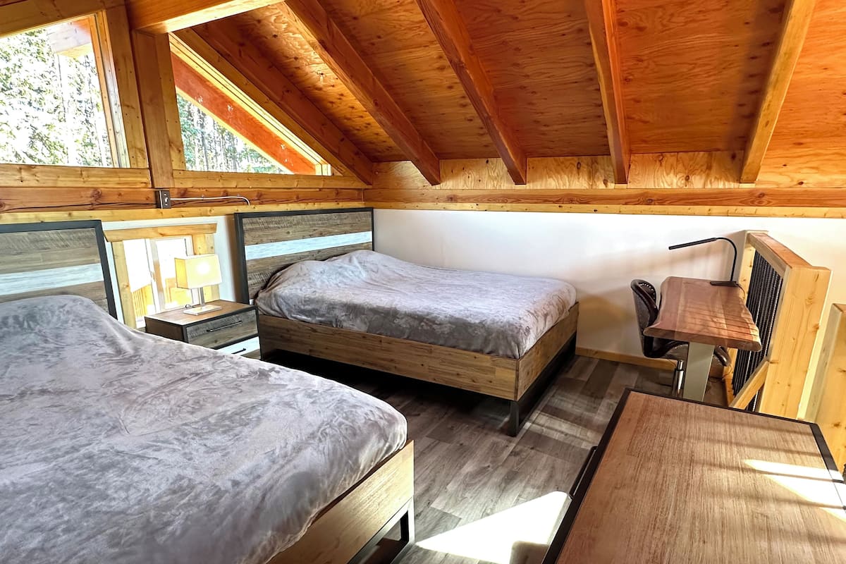 A cabin with two wooden beds, a desk, and a chair.