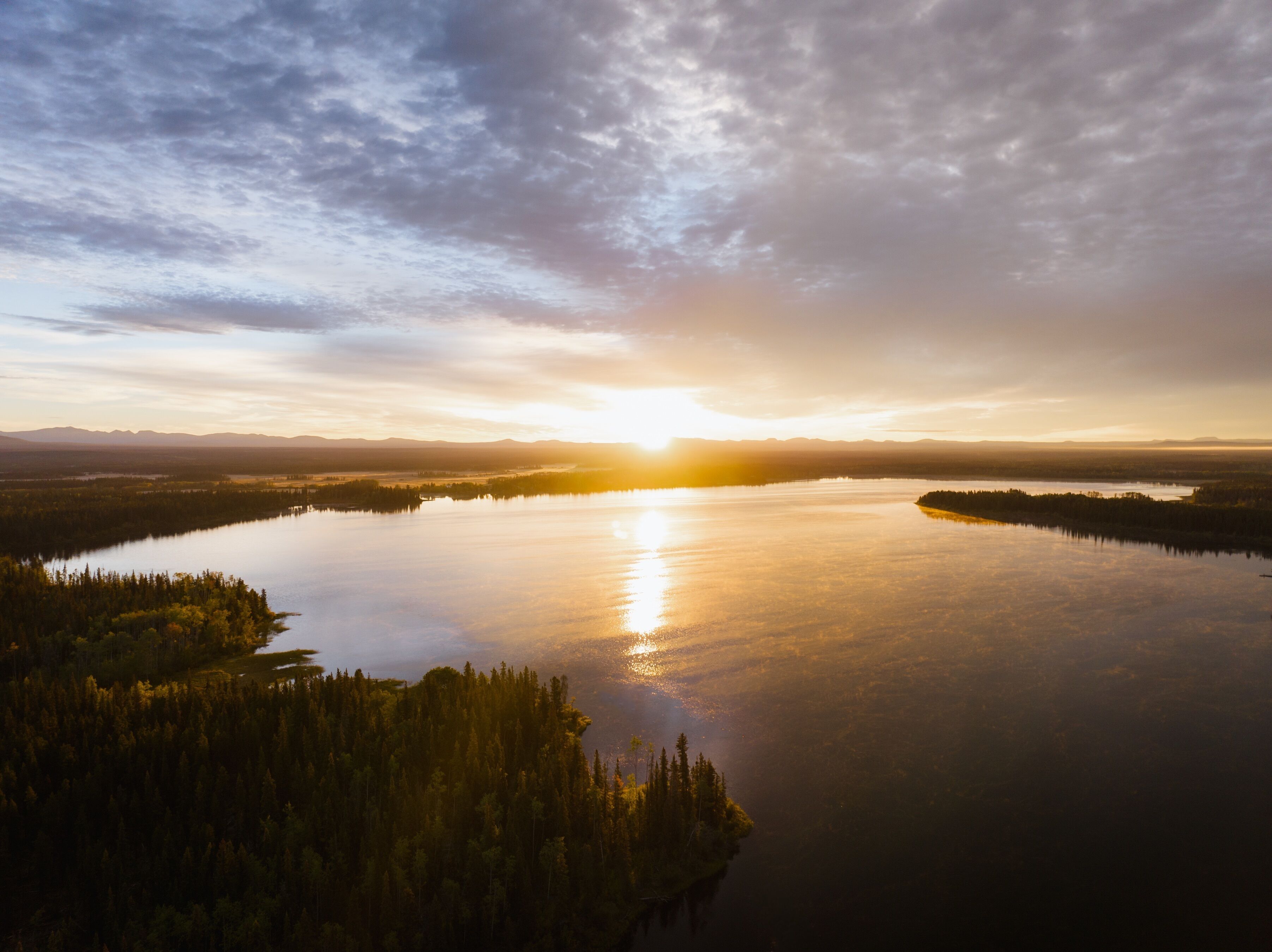 Un lac paisible, entouré d’une forêt dense, avec des montagnes à l’horizon et un ciel nuageux.