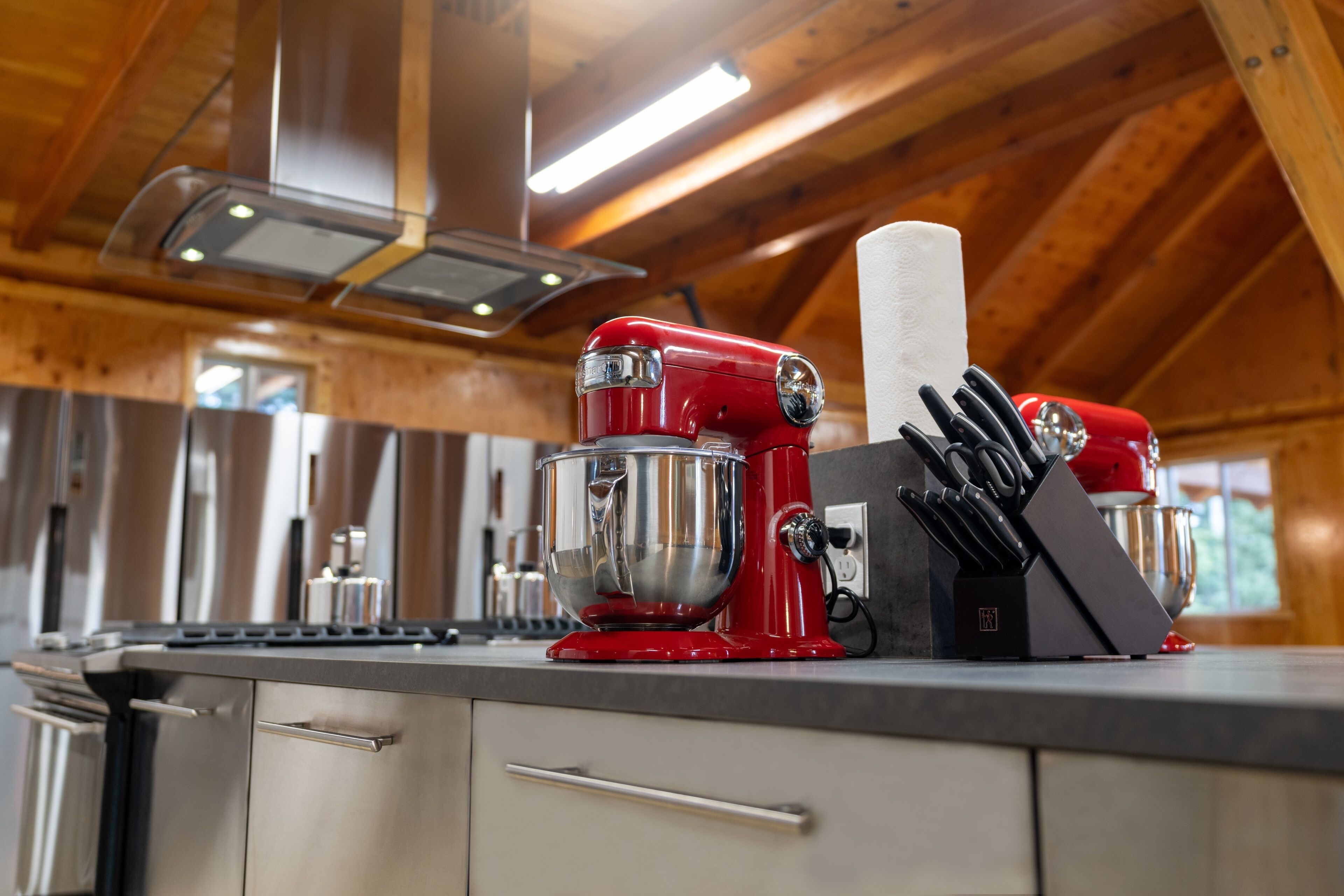 A kitchen with stainless steel appliances, a red mixer, and a knife block on the counter.