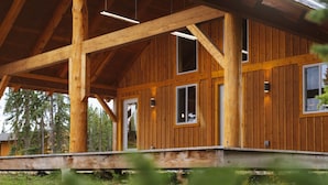 A wooden cabin with a covered porch, large windows, and a visible door. - Red Cariboo Resort (Anahim Lake)