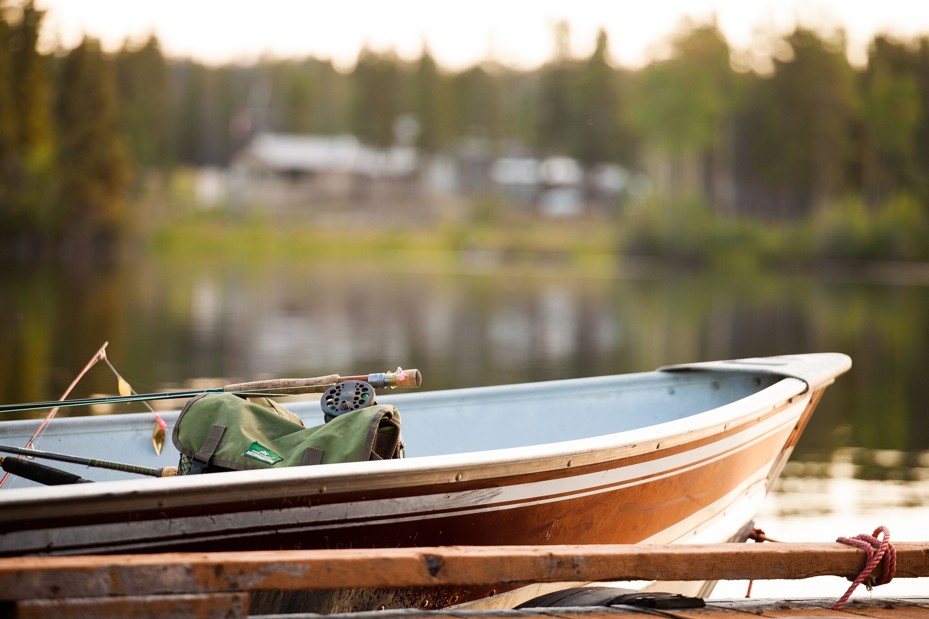 A wooden boat docked at a pier with fishing rods and a green bag on board.