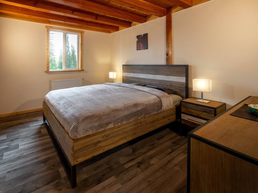 A bedroom with a wooden bed, bedside tables, a nightstand, a window, and a radiator.