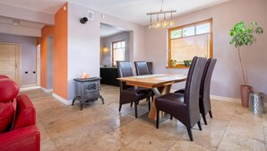 Zona pranzo con tavolo e sedie in legno, un lampadario moderno e una cucina sullo sfondo.