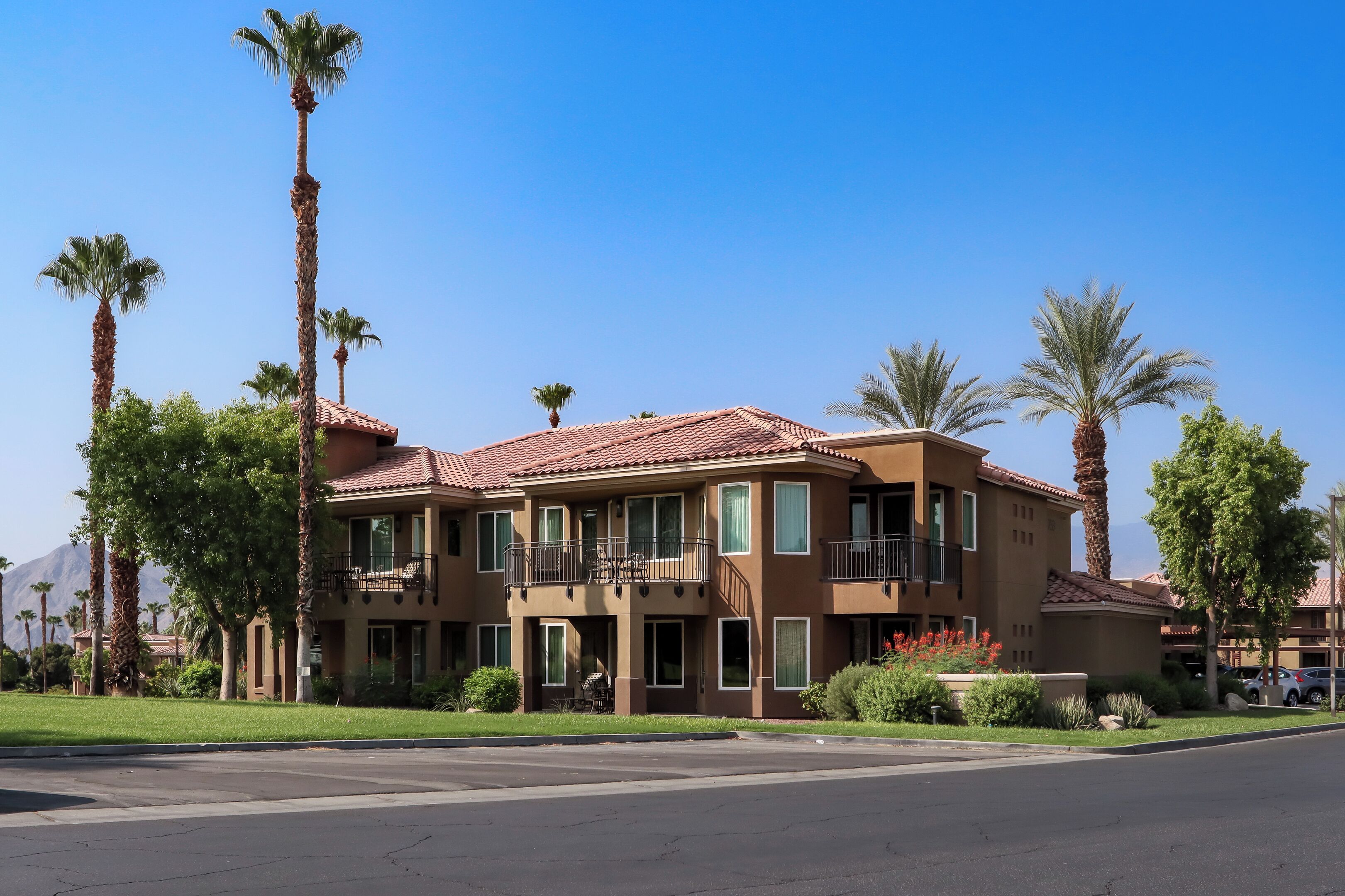 A multi-story hotel with a red-tiled roof, balconies, and palm trees in the vicinity.
