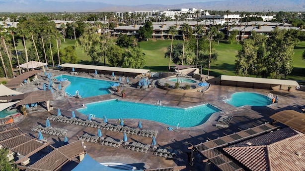 Un complexe hôtelier doté de plusieurs piscines, de chaises longues et d’un terrain de golf en arrière-plan.