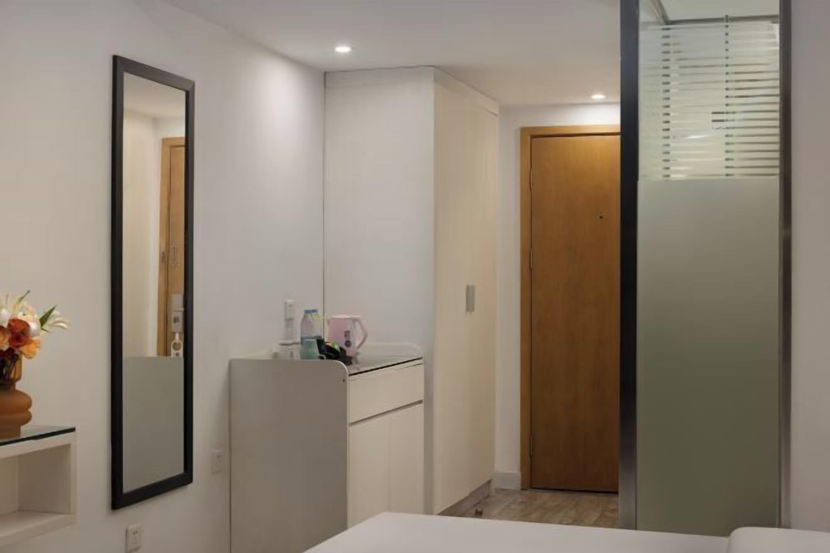 A hotel room with a bed, a mirror, a wardrobe, a small table with toiletries, and a door leading to another room.