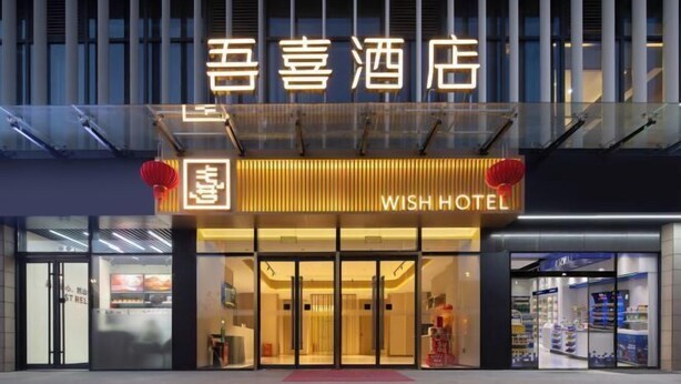 Entrada d'un hotel amb disseny modern, destacant un rètol amb el nom 'WISH HOTEL' i caràcters xinesos a la part superior.