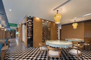 A hotel lobby with a checkered floor, round tables, and a central chandelier.