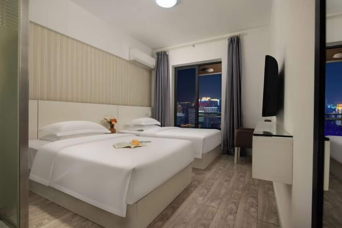 Une chambre d’hôtel avec deux lits, un bureau, une chaise, une télévision et une grande fenêtre donnant sur la ville.