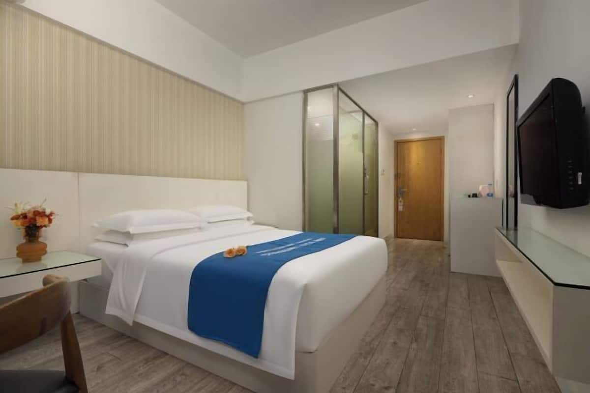 Une chambre d’hôtel moderne équipée d’un lit, d’un bureau, d’une chaise, d’une télévision et d’une porte coulissante donnant sur une autre pièce.