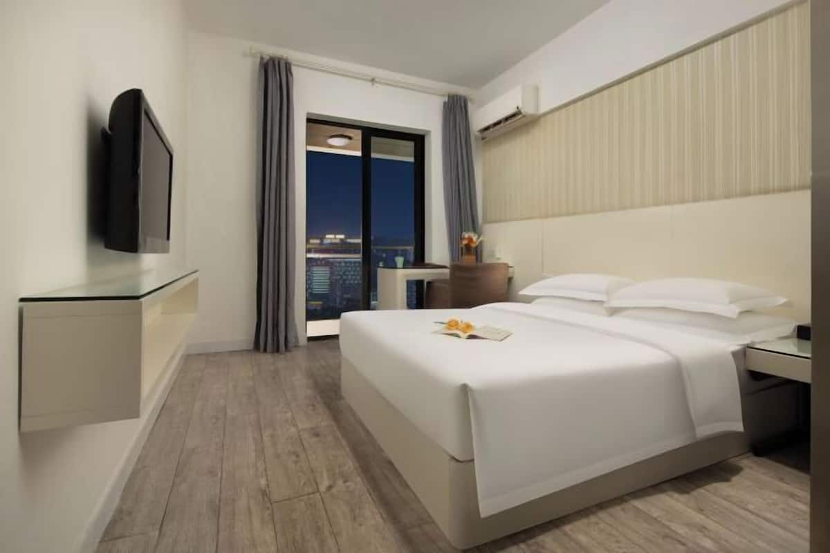 Une chambre d’hôtel avec un lit, une télévision, un bureau et une vue sur la ville la nuit.