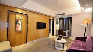 Habitació d'hotel moderna amb una paret d'accent de fusta, televisió de pantalla plana, taula de cafè rodona, sofà morat i zona de menjador amb taula i cadires.