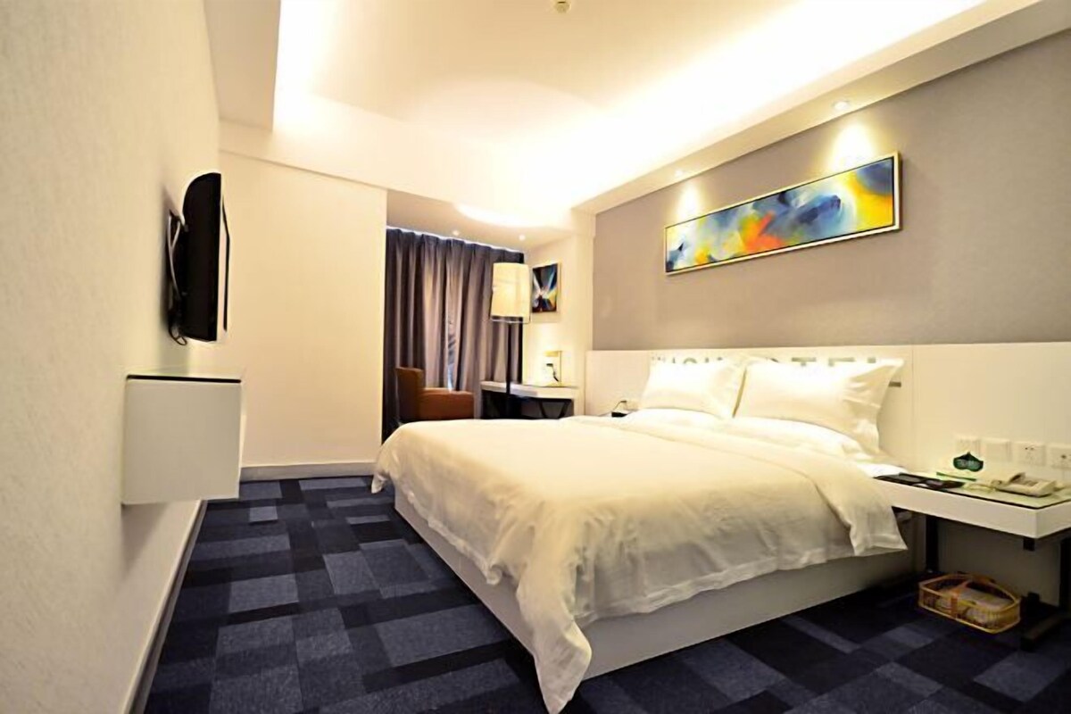 A hotel room with a bed, a desk, a chair, a TV, and a painting on the wall.