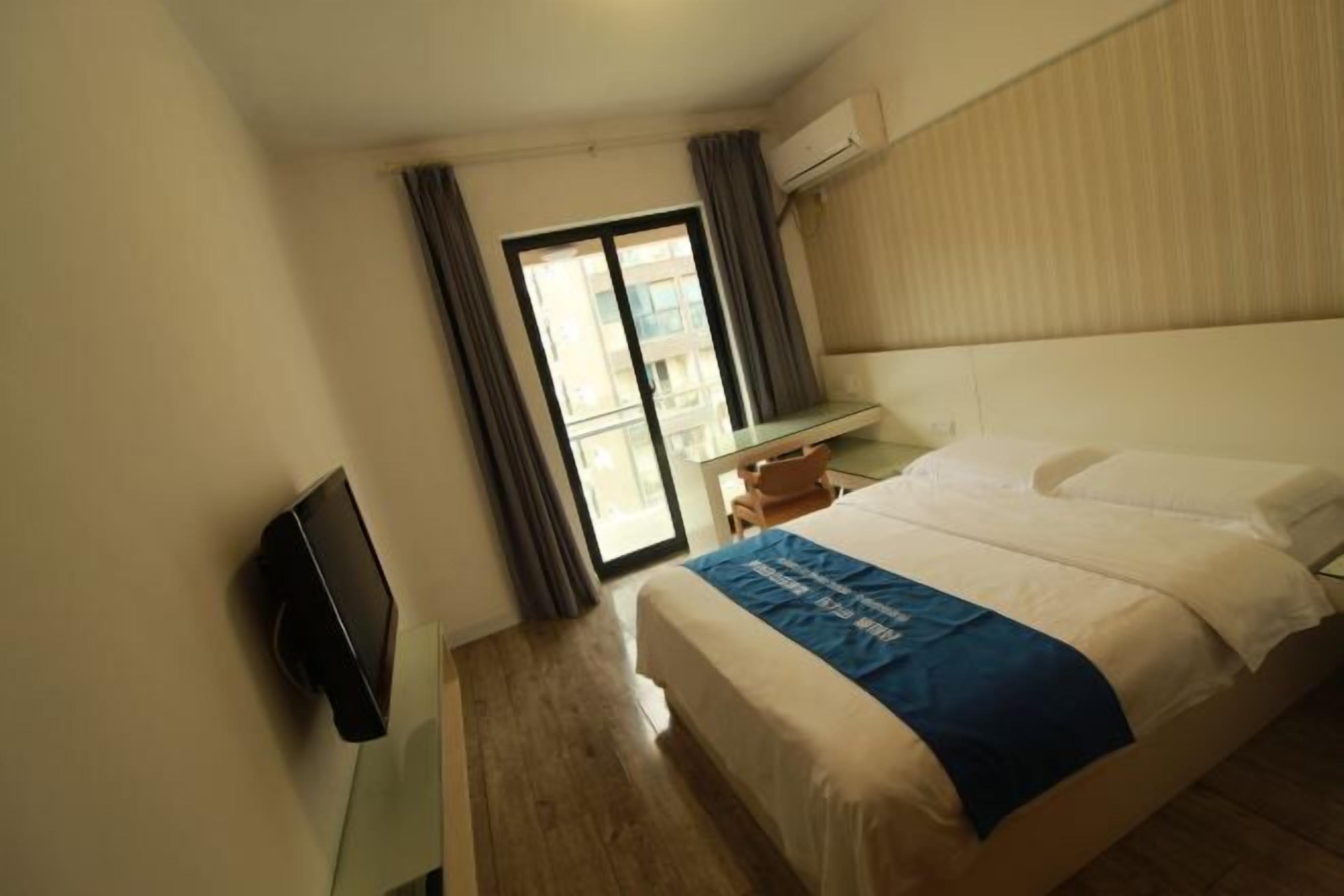 Ein Hotelzimmer mit Bett, Schreibtisch, Flachbildfernseher und einer Schiebetür zum Balkon.