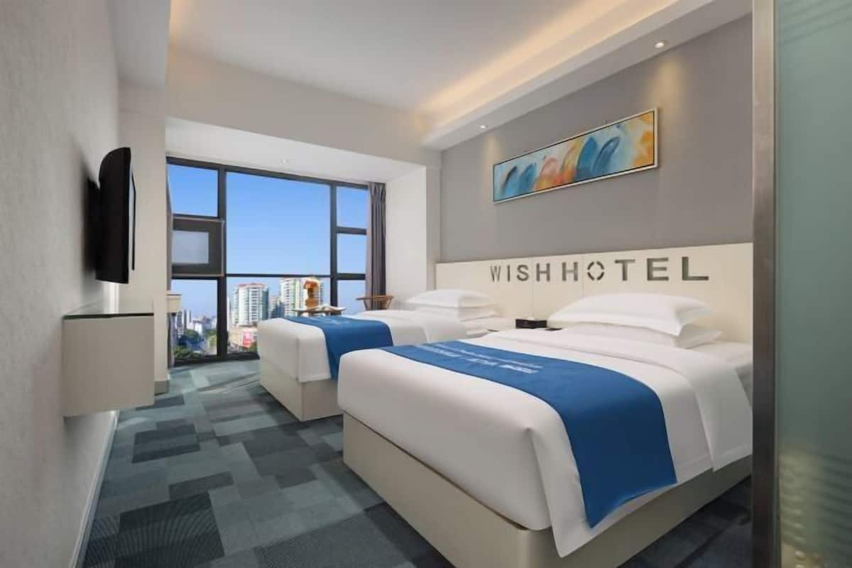 Une chambre d’hôtel avec deux lits, une télévision, une grande fenêtre et une vue sur la ville.
