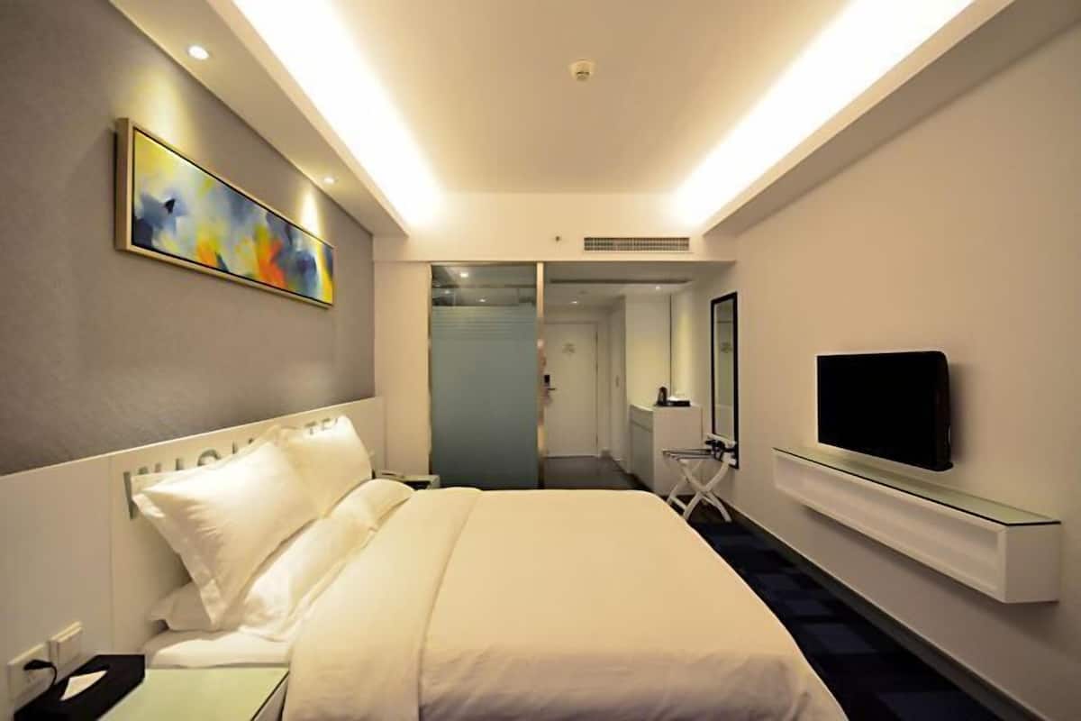 Une chambre d’hôtel avec un lit, un téléviseur fixé au mur et un tableau accroché au mur.