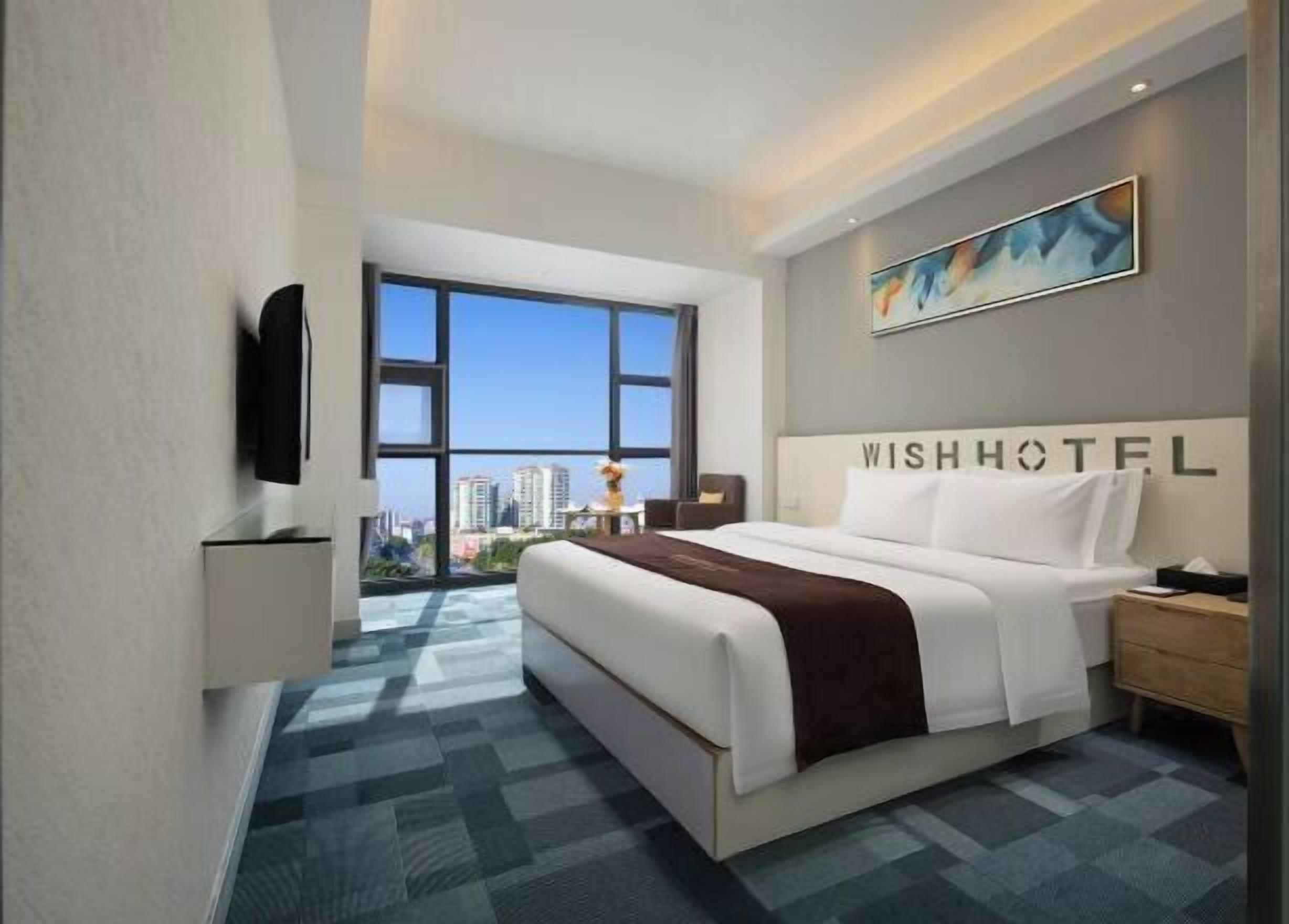 Habitación de hotel con una cama grande, televisión, vista a la ciudad y un cuadro en la pared.