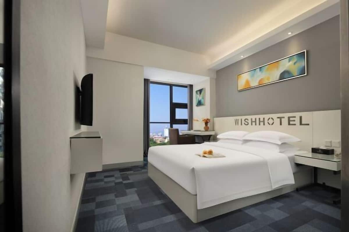 Une chambre d’hôtel moderne dotée d’un grand lit, d’un bureau, d’une chaise, d’une télévision et d’une fenêtre donnant sur la ville.