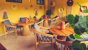 Una habitación con muebles de madera, incluyendo mesas redondas y sillas de mimbre, con una pared amarilla decorada con tapices tejidos.