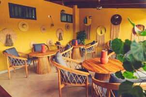 Una habitación con muebles de madera, incluyendo mesas redondas y sillas de mimbre, con una pared amarilla decorada con tapices tejidos.