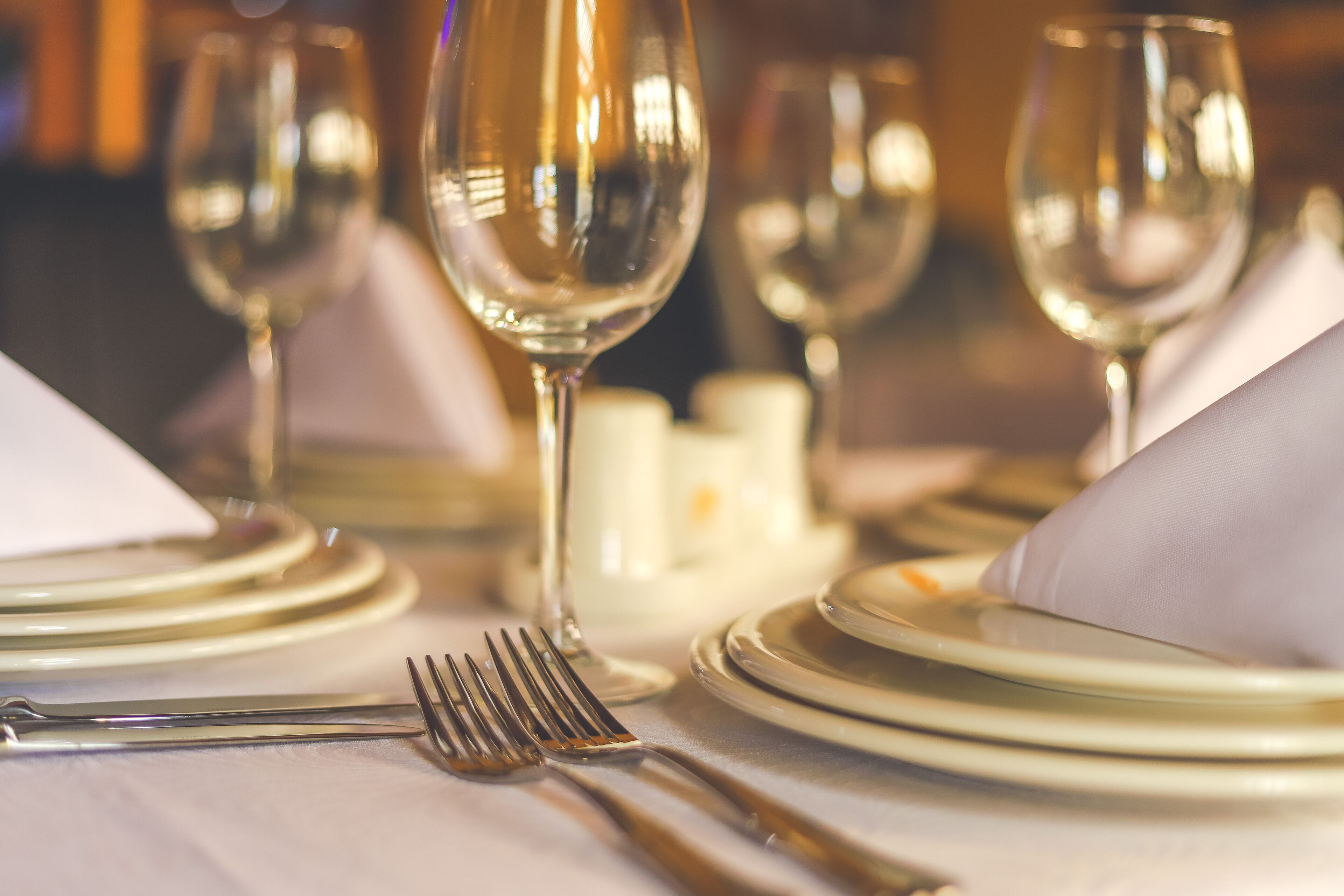 A table set with white plates, gold cutlery, and clear glassware.