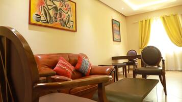 A living room with a brown leather sofa, wooden chairs, a small table, and two paintings on the wall.