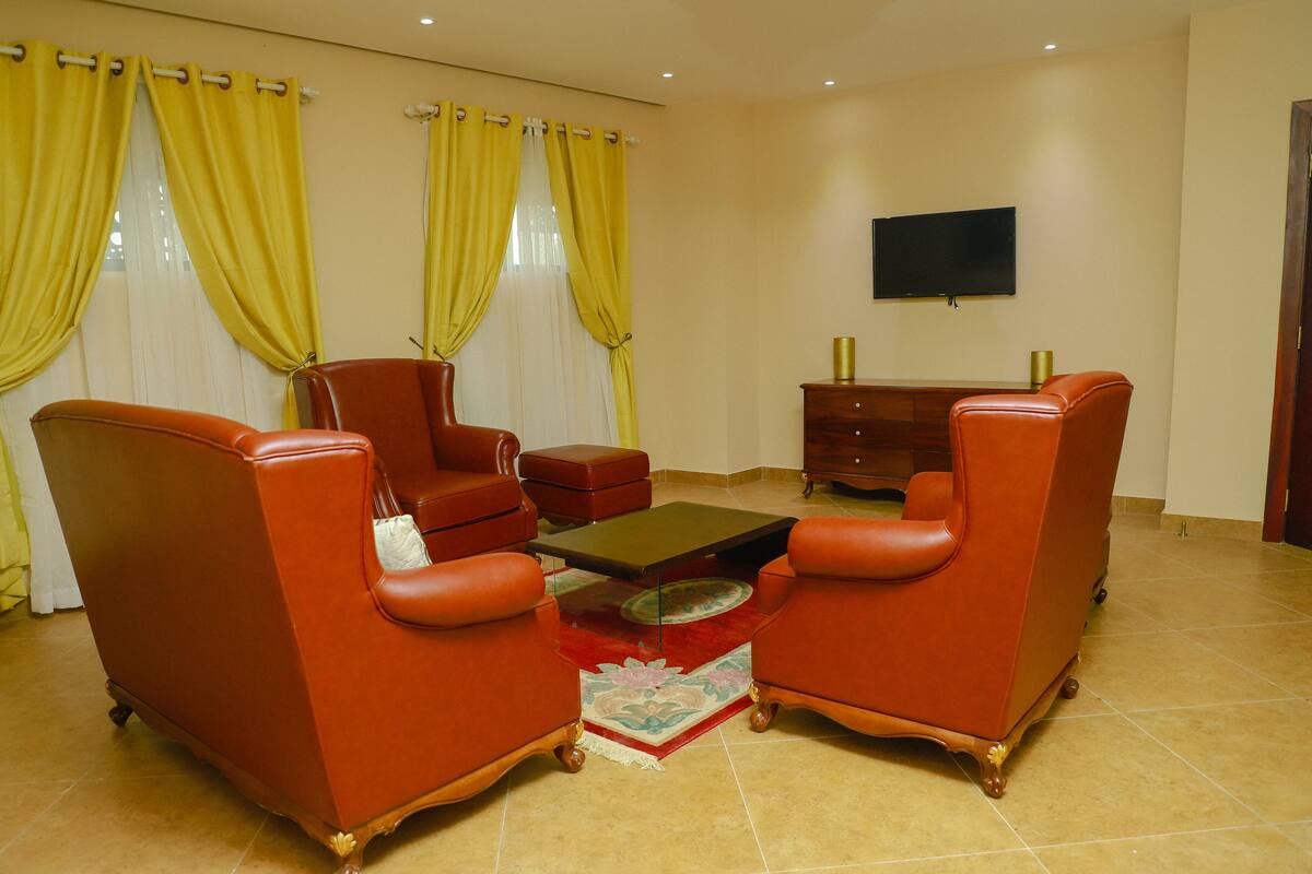 Un salon avec deux fauteuils en cuir rouge, une petite table basse et un téléviseur fixé au mur.