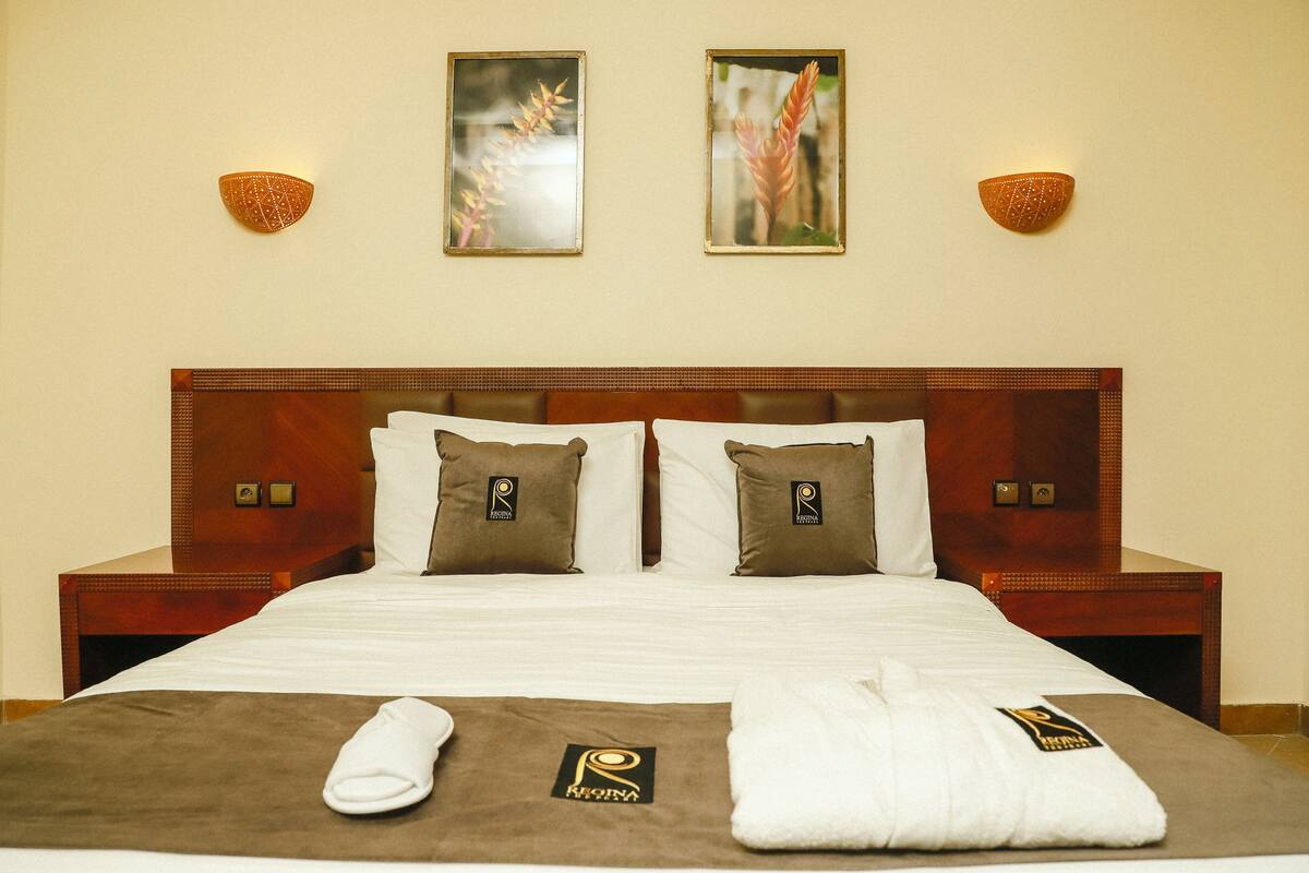Une chambre d’hôtel avec un grand lit, deux lampes fixées au mur et deux tableaux encadrés.