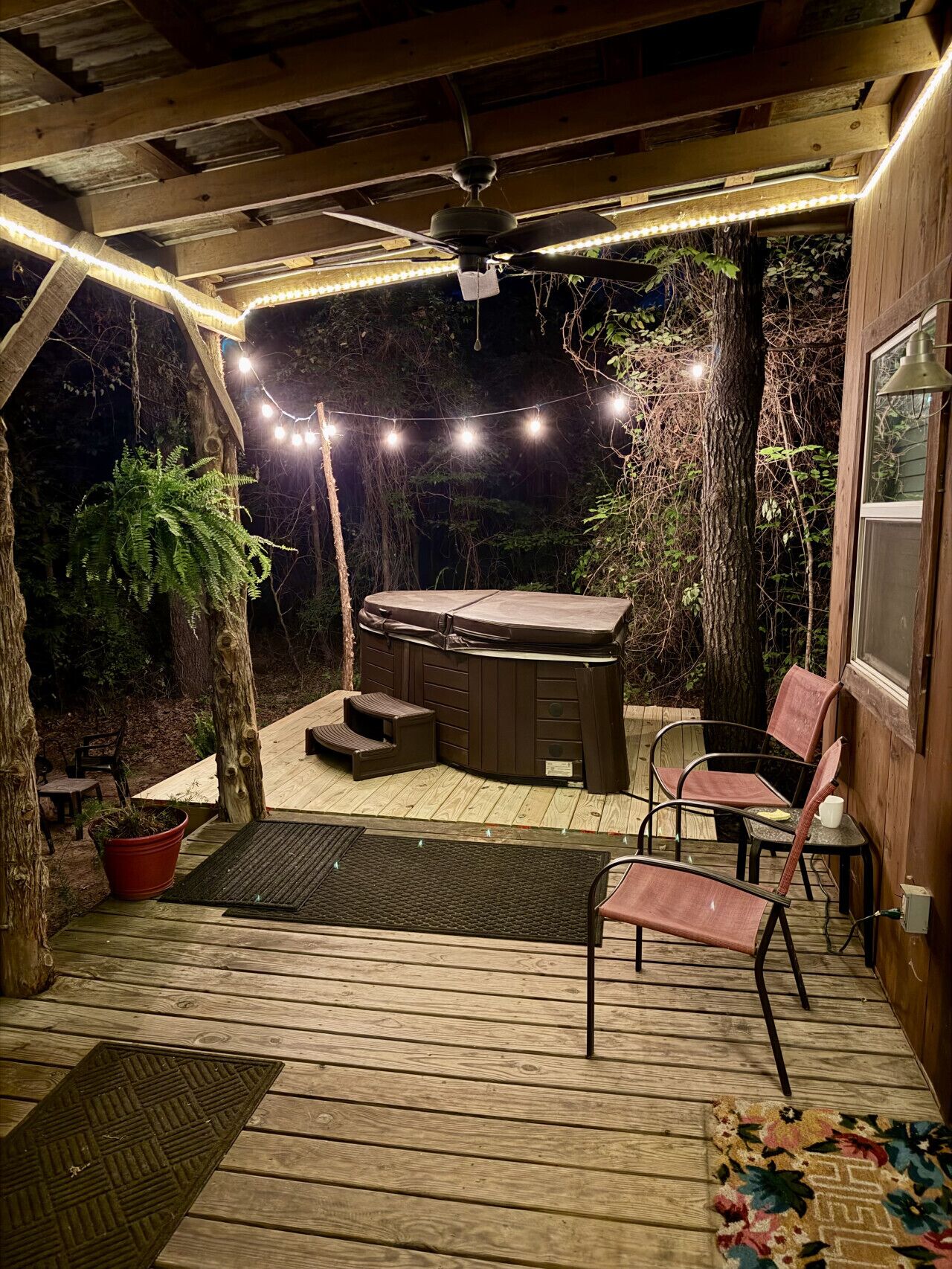 Eine Holzterrasse mit Whirlpool, Stühlen und Lichterkette.