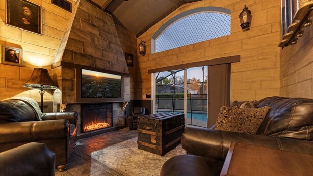 A cozy living room with a fireplace, leather sofas, and a stone wall. - Magical Manor – Castle-Themed Pool Home w/ Hot Tub, Minutes to Disney (Davenport)