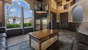 A spacious living room with a wooden coffee table, leather sofas, and a large window offering a view of the neighborhood. - Magical Manor – Castle-Themed Pool Home w/ Hot Tub, Minutes to Disney (Davenport)