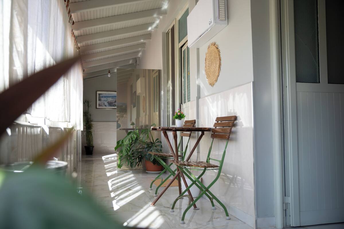 A corridor with a table and chairs, potted plants, and a framed picture on the wall.