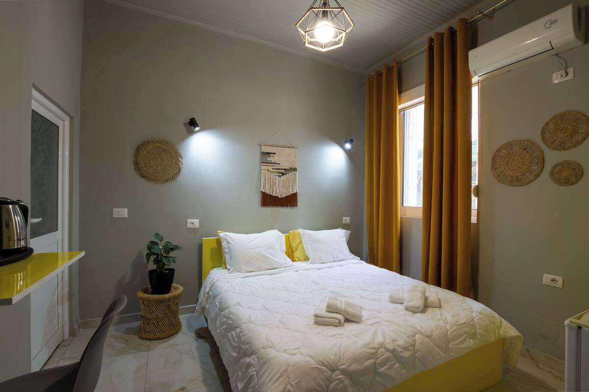 A bedroom with a bed, a potted plant, a wall-mounted light fixture, and a ceiling light.