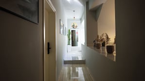 A hallway with a door on the left, a staircase leading to an upper floor, and potted plants on the right. - Hotel Jonian (Sarandë)