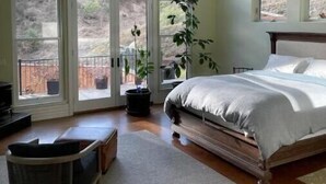 A bedroom with a large bed, multiple windows, a ceiling fan, and a view of the outdoors.