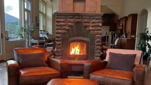 A spacious living room with a stone fireplace, leather sofas, and a large window offering a mountain view.