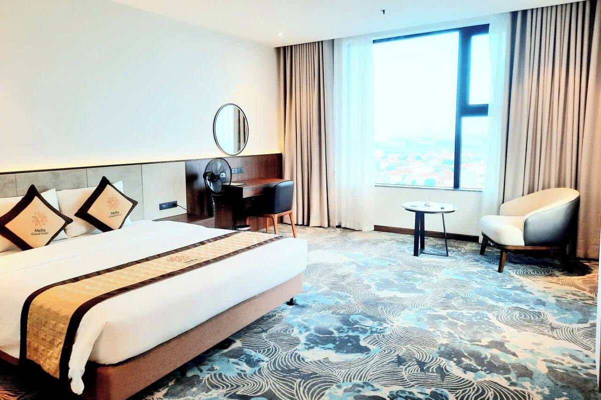 Une chambre d’hôtel avec un grand lit, un bureau, une chaise et une vue sur la ville par la fenêtre.
