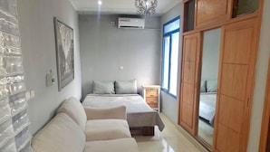 A bedroom with a bed, a wooden wardrobe, a nightstand, a sofa, and a wall-mounted air conditioner. - Mike's Flat hotel (Kinshasa)