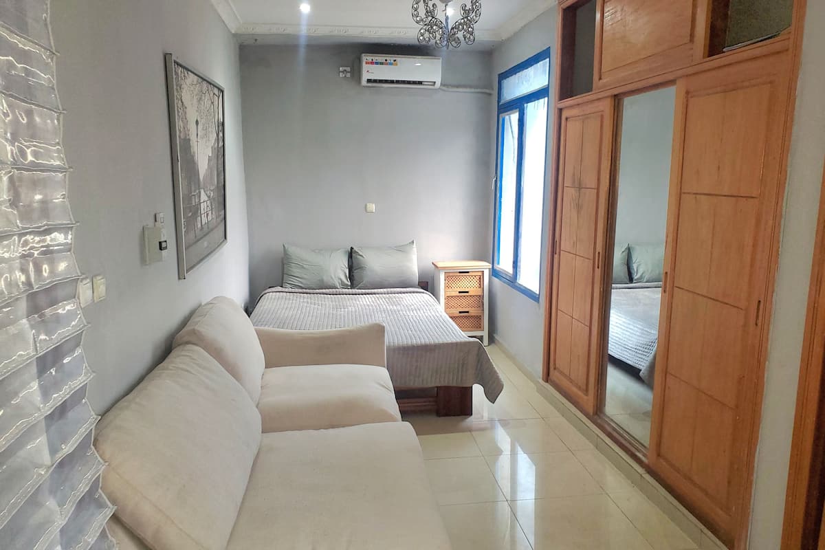 A bedroom with a bed, a wooden wardrobe, a nightstand, a sofa, and a wall-mounted air conditioner.