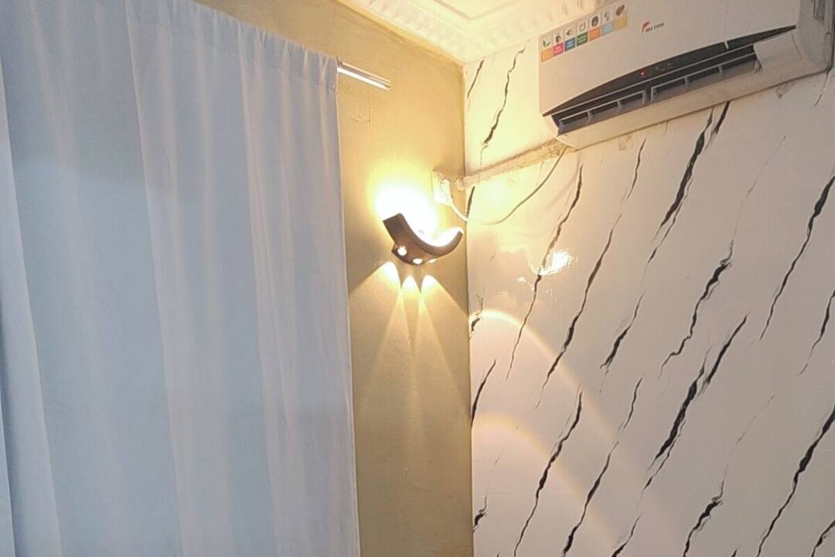 A bedroom with a bed, floral bedding, a wall-mounted air conditioner, and a curtain.