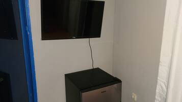 A small room with a flat-screen TV mounted on the wall, a black refrigerator, and a blue door.