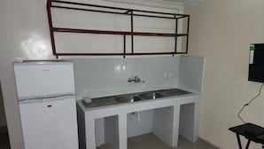 A compact kitchenette with a refrigerator, double sink, and a small black table. - Mike's Flat hotel (Kinshasa)