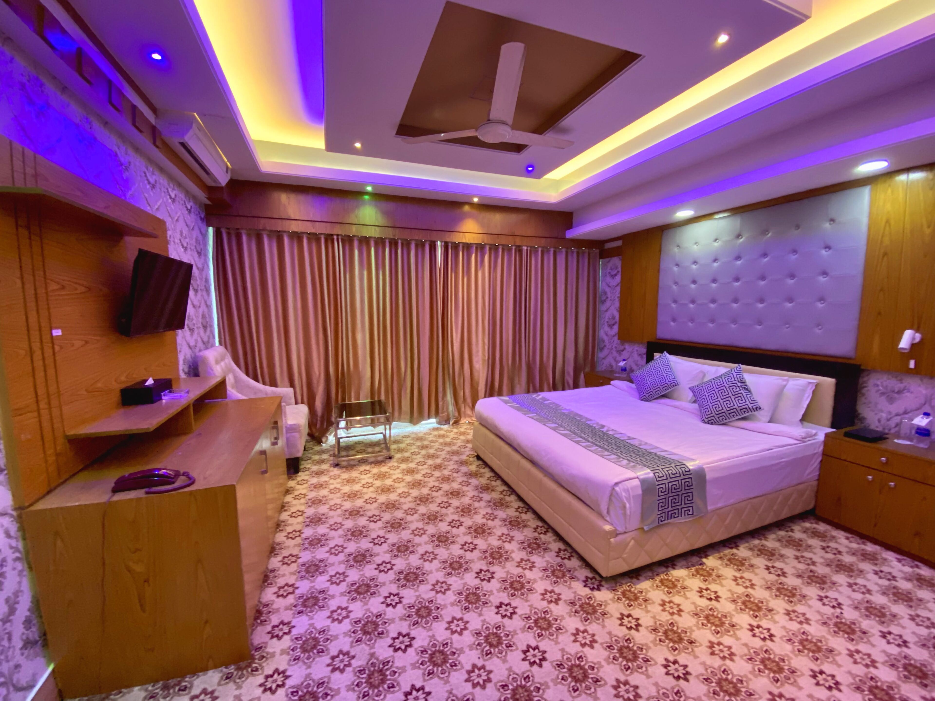 Une chambre moderne avec un grand lit, un téléviseur fixé au mur, un bureau et un ventilateur de plafond.