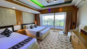 A hotel room with two beds, a sofa, a desk, and a balcony with a city view.